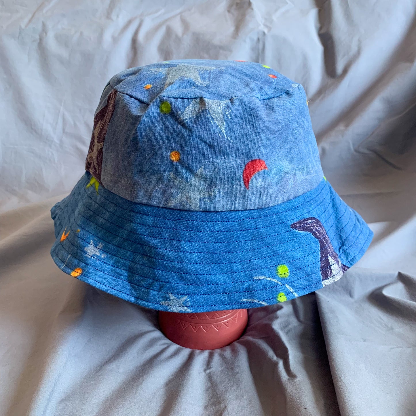 A blue bucket hat with stars styled on a pink stone head against a blue background