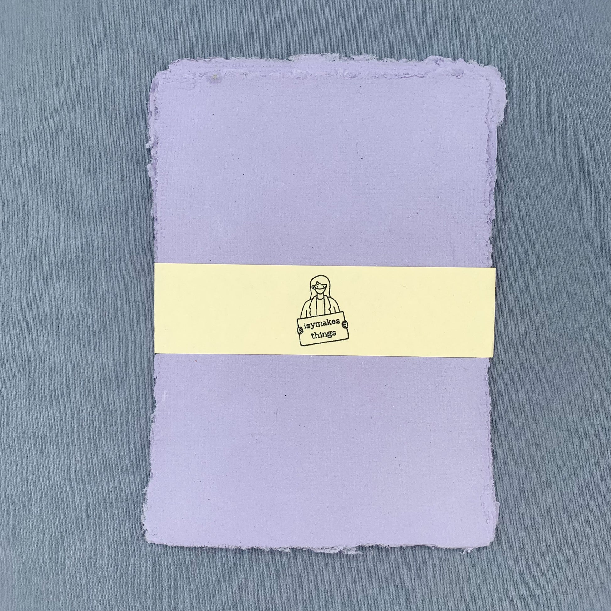 a stack of purple sheets of paper with a cream coloured isymakesthings logo sleeve around them against a blue background