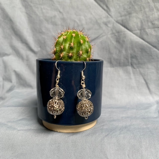 Shiny ball stacked earrings hang off a dark blue cactus pot