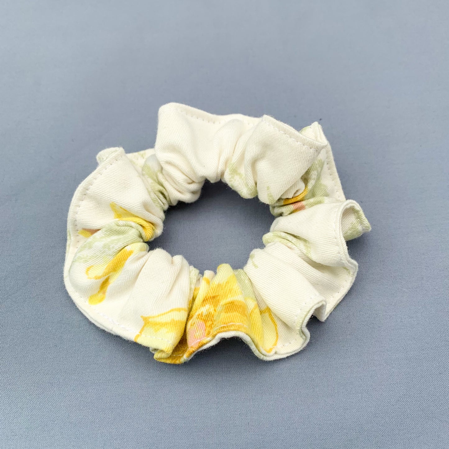 a white & yellow floral scrunchie laying on a blue background