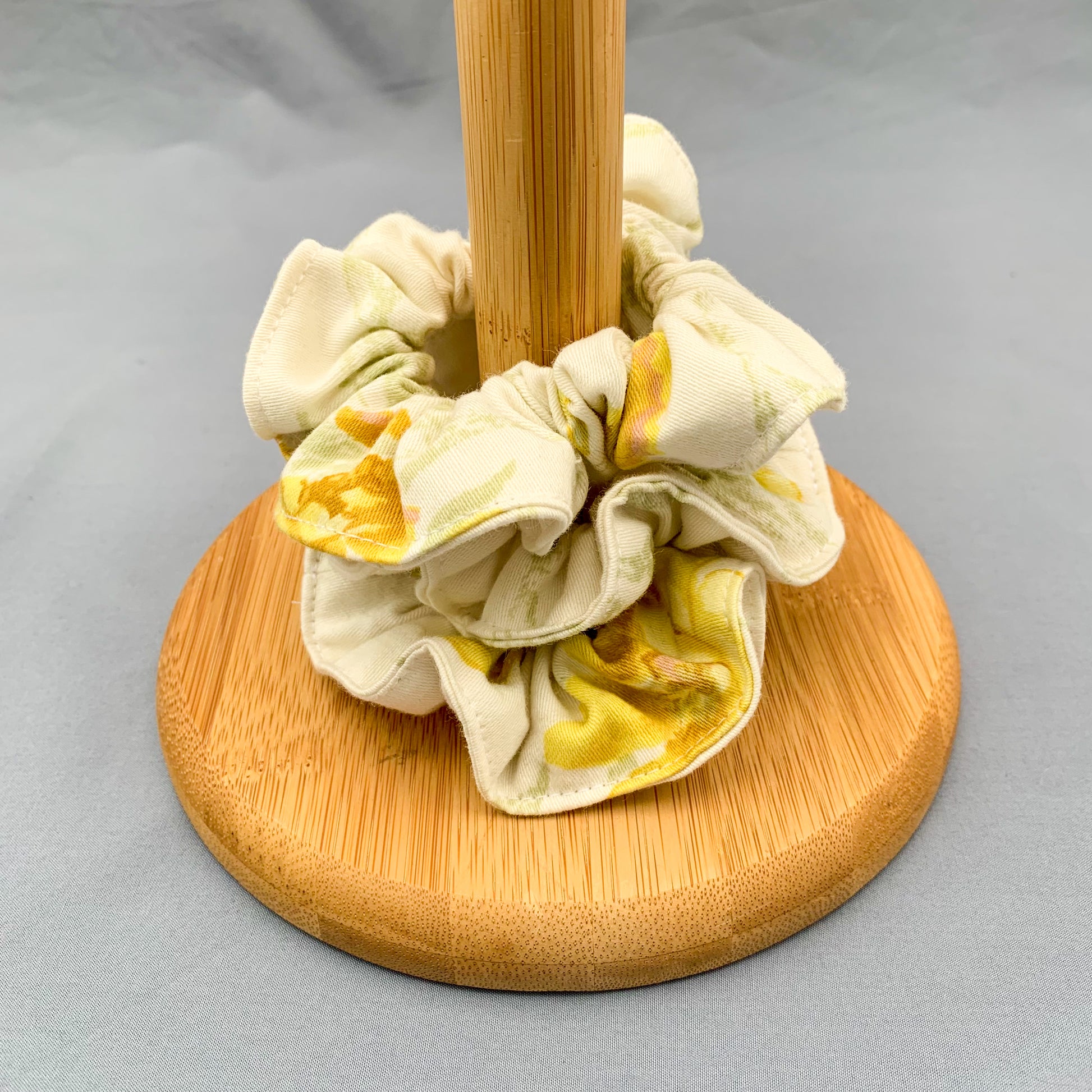 white & yellow floral scrunchies on a wooden holder on a blue background