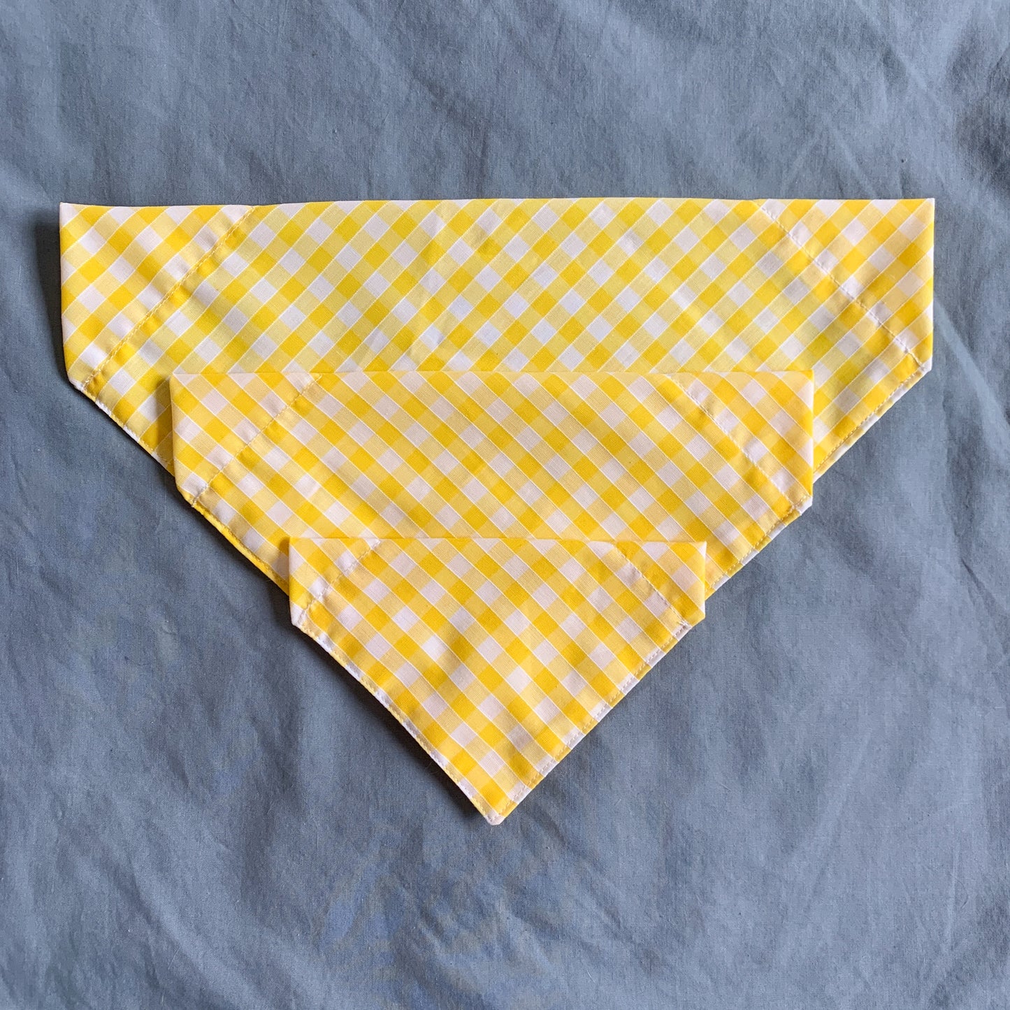 three different sized yellow gingham triangle bandanas sit atop each other